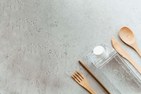 Top view of eco friendly utensils placed near bottle with water and mint leaf on gray stone surfaceの写真素材