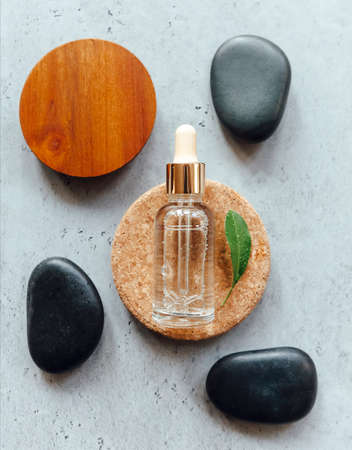 Top view of bottle of essential oil placed on wooden and stone circles near fresh leaf and smooth pebblesの写真素材