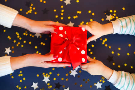 Top view of female and little girlreceiving red box with bow together above dark navy background with star confettiの写真素材