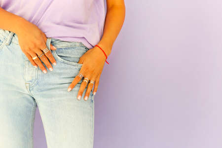 Unrecognizable crop female wearing t shirt and stylish jeans standing on lilac background and demonstrating various silver ringsの写真素材