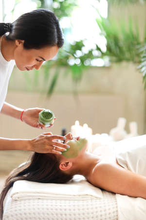 Beautiful relaxed woman having green clay face mask in spa salonの写真素材