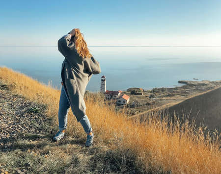 Side view of unrecognizable female standing on grassy hill and admiring amazing seascape during...