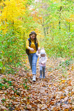 Mother and daughter play in autumn park. Parent and child walk in the forest on a fall dayの写真素材