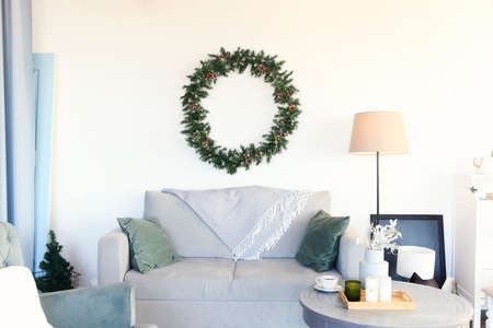 Spruce wreath hanging on wall above gray cozy sofa with table and armchair near in living roomの写真素材