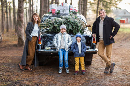Smiling adult man and woman with kids in warm clothes standing at vintage car with Christmas presentsの写真素材