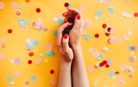 From above of anonymous female with stylish manicure with red nail polish on yellow background with colorful confettiの写真素材
