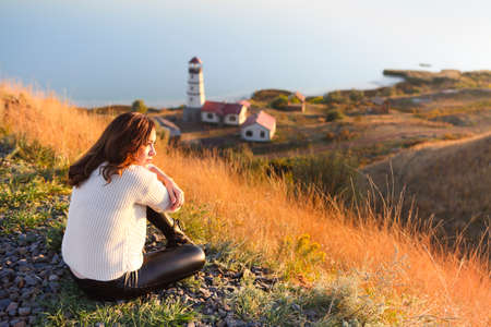 Young woman with near the Lighthouse and blue sea on background in autumn sunsetの写真素材