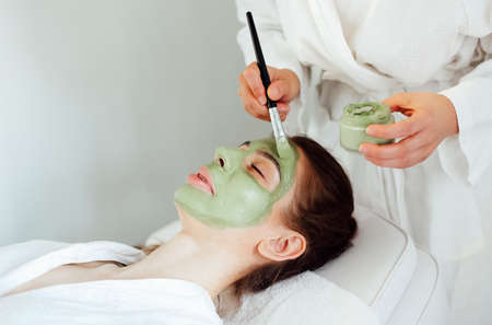 Beautiful relaxed woman having green clay face mask in spa salonの写真素材