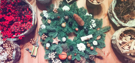 Top view of decorated Christmas green fir wreath placed on wooden table with baskets of red berries...