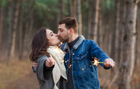 Handsome man and woman in warm clothes outstretching hands with burning sparkles while kissing with...