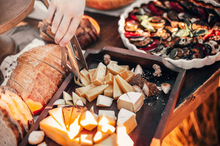 High angle of crop anonymous person with tongs taking piece of cheese from tray placed on buffet table during outdoor eventの写真素材