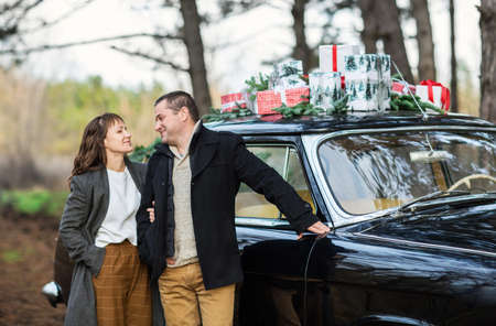 Loving man and woman by the retro car with Christmas gifts on roof in park