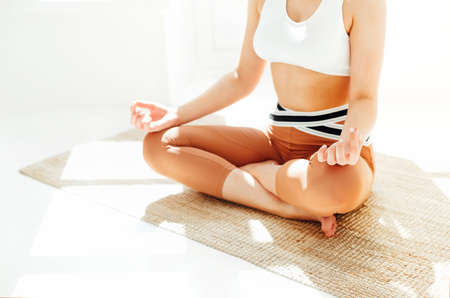Back view of unrecognizable female in sportswear sitting with crossed legs and mudra hands on mat...