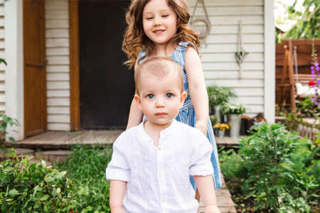 Cute little brother and sister near the country house and relaxing in rural area during summer holidayの写真素材