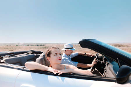 Back view of unrecognizable couple in hats enjoying freedom while traveling in convertible car through desert grassy countryside in summer dayの写真素材
