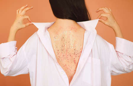 Back view of young female in white clothes revealing back with shiny mask against brown background