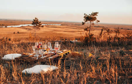 Set of elegant glassware placed on plank wooden table with floral arrangement on grassy meadow during festive autumn picnicの写真素材