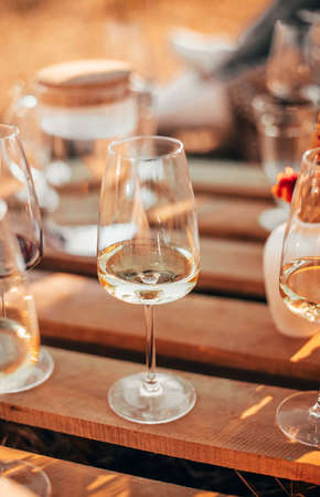 Set of elegant glassware placed on plank wooden table with floral arrangement on grassy meadow during festive autumn picnicの写真素材