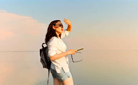 Side view of carefree female standing near sea and covering face from sun at sundownの写真素材
