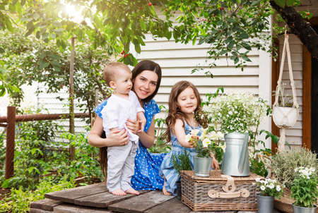 Young delighted mother sitting in armchair with adorable little siblings on terrace of country house and relaxing together during weekendの写真素材