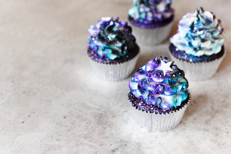 High angle of yummy cupcakes with galaxy colored cream and star shaped decoration placed on gray tableの写真素材