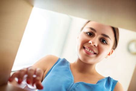 From below happy young female smiling and looking inside carton box while opening ordered goods