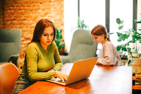 Side view of happy woman smiling and browsing laptop while sitting at table and working on remote...