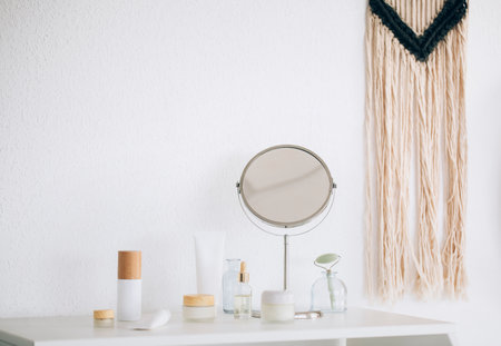 Composition of various cosmetic supplies and round mirror placed on table against white wallの写真素材