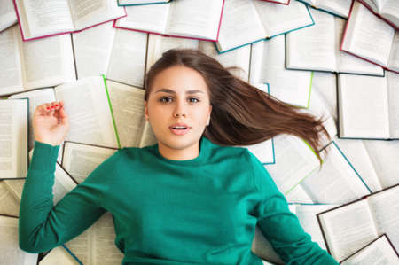 Top view of brunette female student lying on books and reading during exam preparationの写真素材