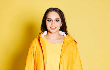 Happy young female in trendy yellow sweatshirt and coat smiling brightly against yellow background