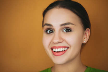 Positive female laughing happily on brown background in studio and looking at camera