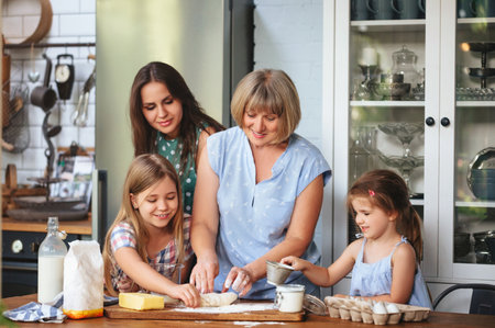 Happy adult and mature women cooking together with cute girls at table in kitchen