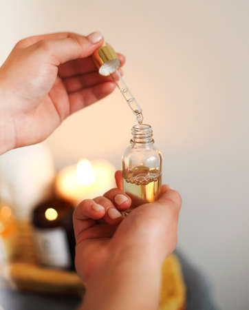 Crop masseuse using pipette with massage oil placed on tray with assorted spa supplies in salon