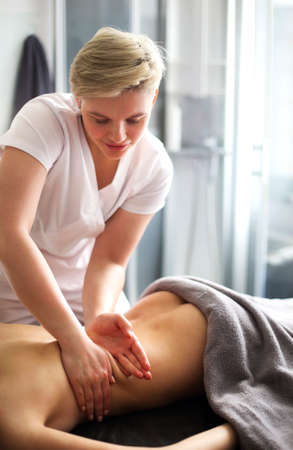 Faceless master giving massage of back and shoulder muscles to anonymous woman lying on table in spa salonの写真素材