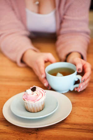 High angle of blurred unrecognizable female sitting at table with sweet delicious cupcake and cup of aromatic tea in cafeの写真素材