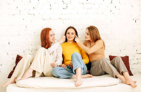 Optimistic young women smiling and touching face of stylish girlfriend while resting near rough...