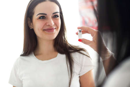 Professional female beautician showing filler in glass bottle for woman before injection in beauty clinicの写真素材