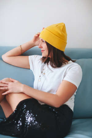 Side view of barefoot female in trendy clothes looking at camera while sitting on blue couch against gray backgroundの写真素材