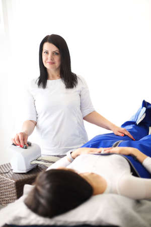 Mature woman with apparatus for anti cellulite massage at couch with female customer in salon