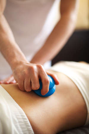 Faceless masseur rubbing back of customer with help of rubber vacuum cup working in salonの写真素材