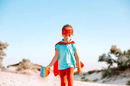 Happy Superhero kid running on the beach holding silicone toy in her handの写真素材