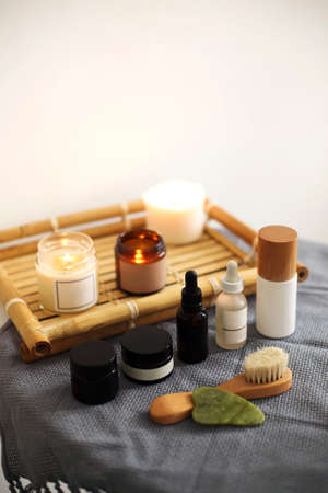 Burning candles and containers with various skincare cosmetics placed on table at home