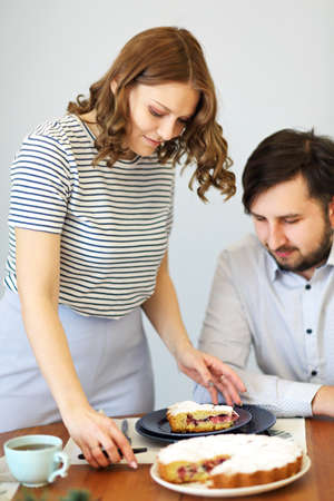Woman cutting pie and man drinking beverage while having breakfast together at table in kitchenの写真素材
