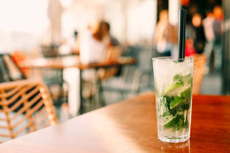 High angle of glass with sweet cold cocktail and straws placed on table in bar on summer day. Mojito cocktail in bar with crowd peopleの写真素材