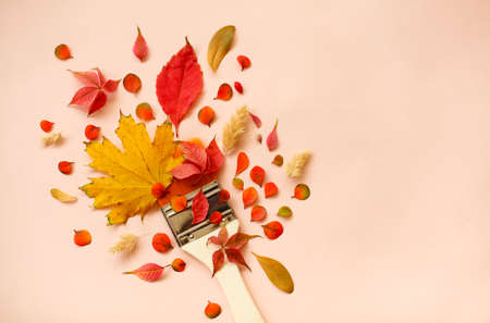 Top view of paintbrush surrounded with red and yellow dry autumn leaves on peach background