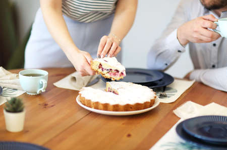Woman cutting pie and man drinking beverage while having breakfast together at table in kitchen. Close upの写真素材