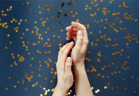 From above of anonymous female with stylish manicure with white nail polish on navy blue background...