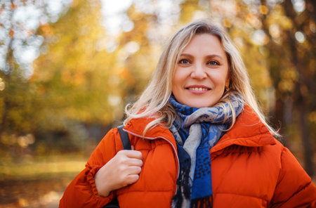 Delighted female in outerwear smiling on sunny weekend day in autumn park