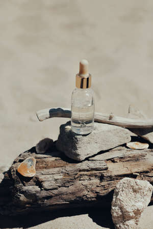 Top view of bottle with aromatic essential oil placed on rough wood near stones and twigs on sandy...
