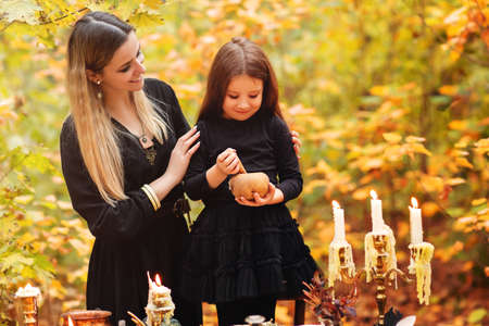 Happy woman and girl crushing herbs in mortar while preparing magic potion during Halloween...